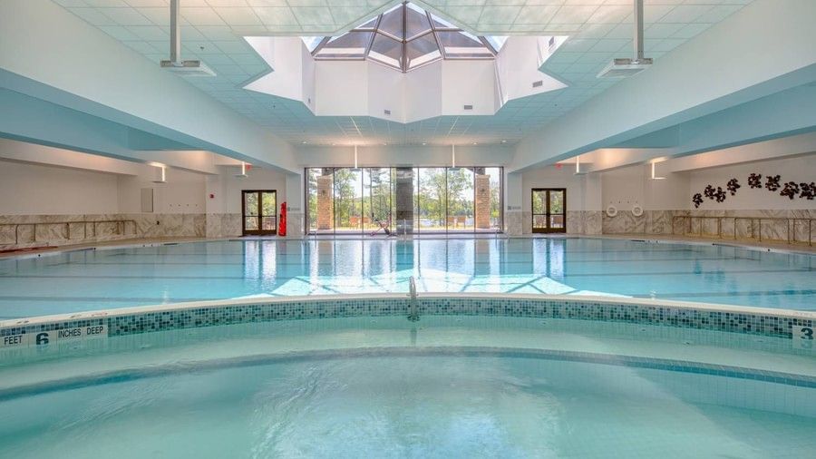Bright indoor swimming pool with a large pyramid-shaped skylight and double glass doors leading to the outdoors