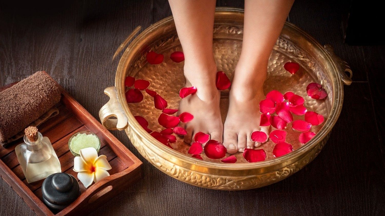 A foot soak with rose petals in a copper bowl, with aromatherapy oils and stones nearby.
