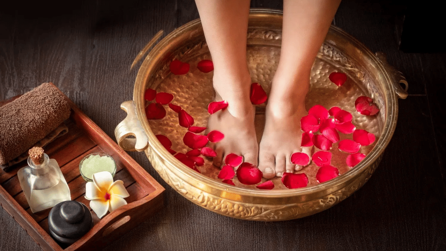 A foot soak with rose petals in a copper bowl, with aromatherapy oils and stones nearby.