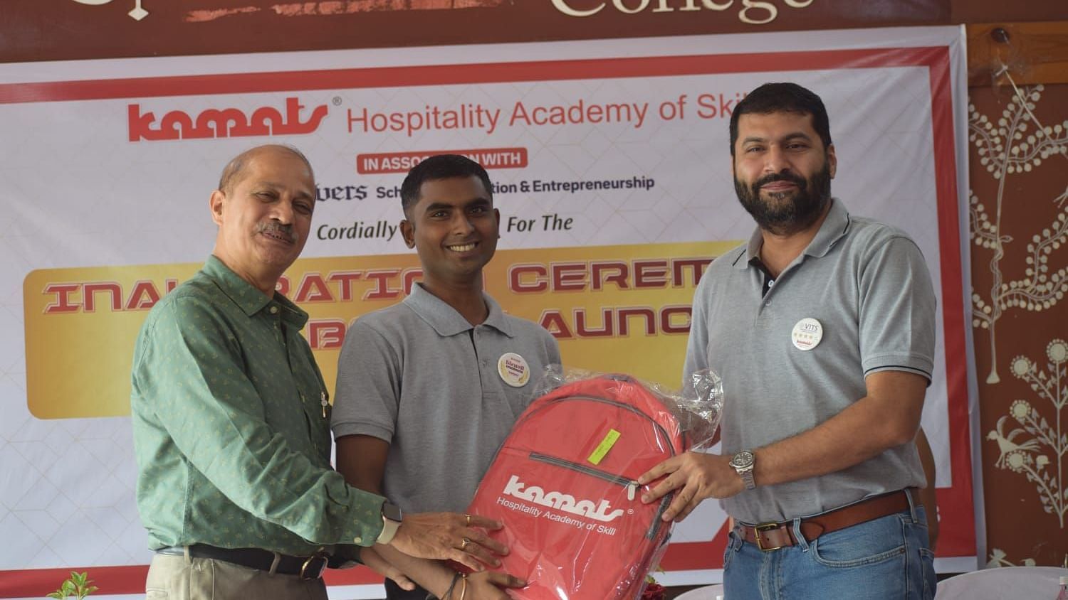 Inauguration ceremony with a person receiving a branded backpack - Kamats India