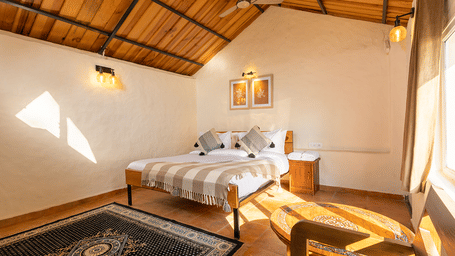Bright cottage bedroom with natural sunlight, wooden ceilings, and traditional rugs at Maati Resort By The Lake Hill, Jeolikote.