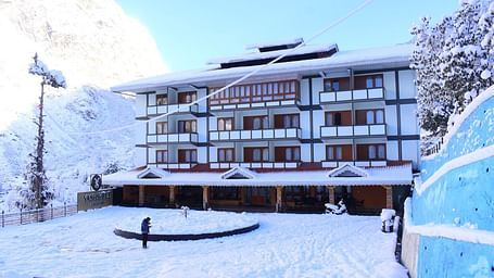Image of the hotel covered with snow along with mountains on all side and trees covered with snow  | Yashshree Lachung
