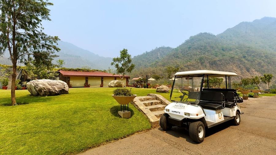 A golf cart parked on a gravel path in a lush landscape in the background and mountains in the distance.