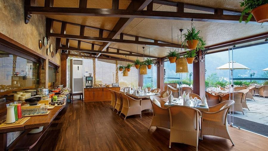 A spacious restaurant with a wooden floor and exposed wooden beams on the ceiling. Large windows offer views of the outdoors.