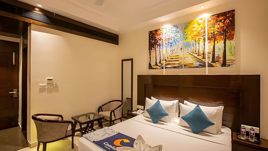 Bedroom at Inde Reva Resorts Rishhikesh with a double bed, blue cushions, chairs, painting, and ceiling lights.