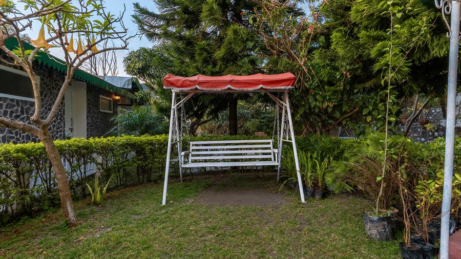 A relaxing white swing bench set in the lush landscaped gardens at Maati Resort By The Lake Hill, Jeolikote.