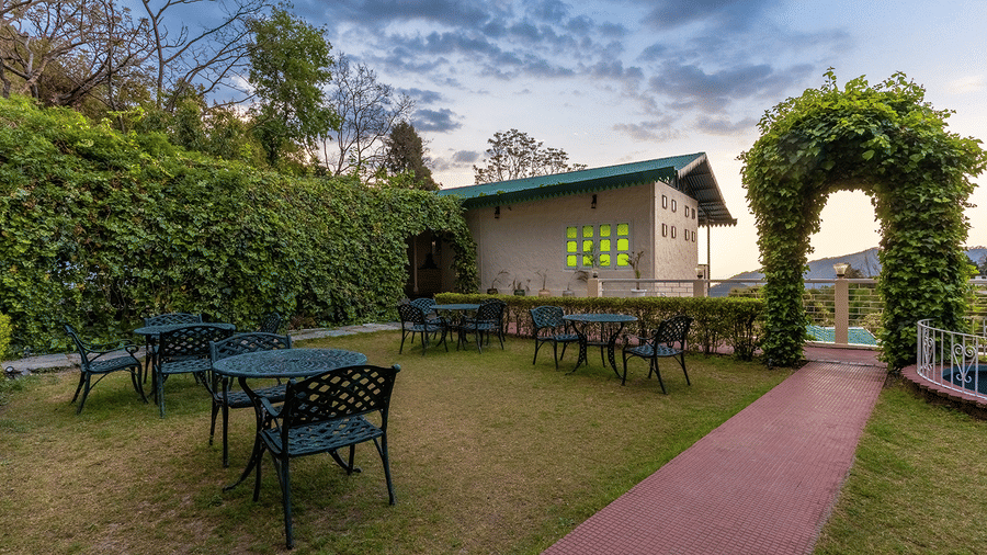 Tranquil outdoor garden seating with iron tables and chairs surrounded by greenery at Maati Resort By The Lake Hill, Jeolikote.