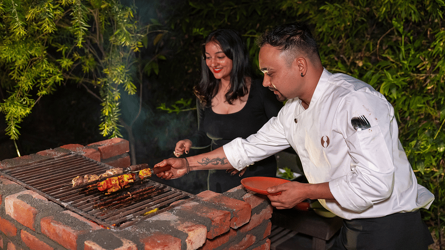 Chef and guest enjoying an outdoor live barbecue grilling session at night at Maati Resort By The Lake Hill, Jeolikote.