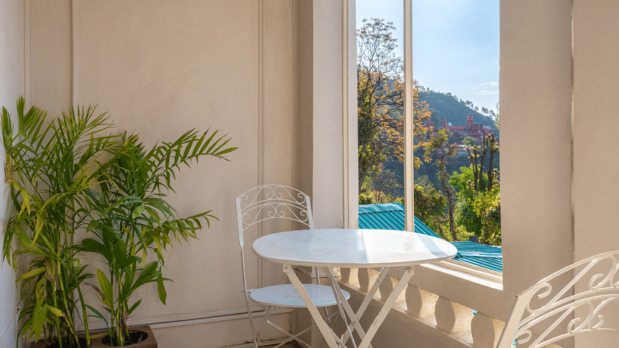 A cosy white bistro set on a private balcony overlooking the hills and greenery at Maati Resort By The Lake Hill, Jeolikote.