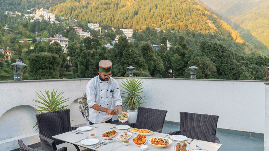 A chef arranging food on an outdoor dining table with chairs, overlooking a mountain landscape at Quality Inn.