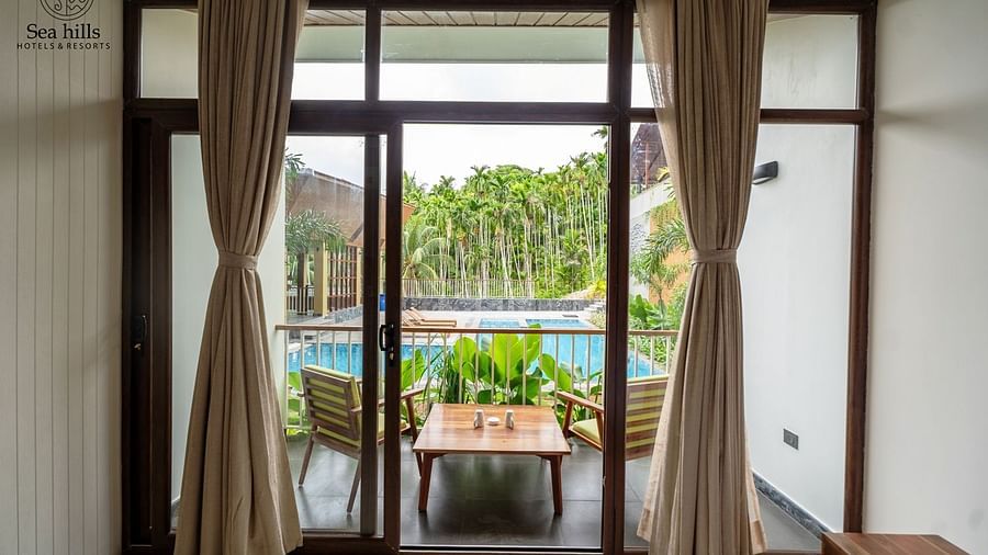 Room with large glass windows offering a scenic view of the pool, accompanied by comfortable wooden furniture - Sea Hills Resort, Swaraj Dweep (Havelock)