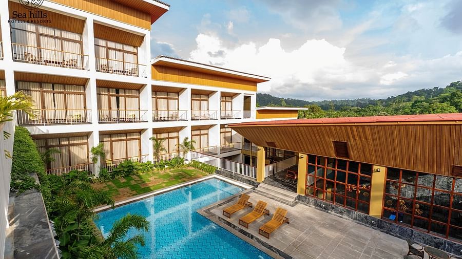 An exterior shot of a large resort building with multiple floors and an outdoor swimming pool, set against a hilly landscape. - Sea Hills Resort, Swaraj Dweep (Havelock)