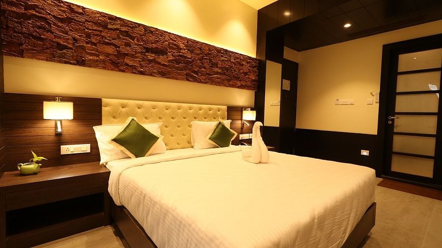 A spacious hotel bedroom with a large bed, a comfortable armchair, and a view of the outside through a large glass door, featuring modern design elements - Sea Hills Hotels, Sri Vijaya Puram (Port Blair)