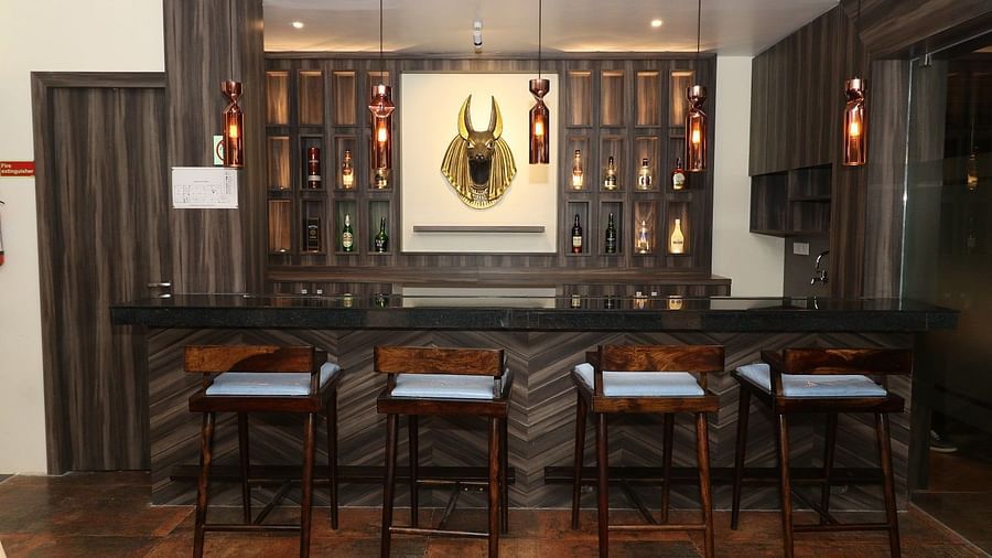A well-stocked bar area with dark wooden counters, high bar stools, and bottles displayed on shelves, illuminated by hanging lights - Sea Hills Hotels, Sri Vijaya Puram (Port Blair)