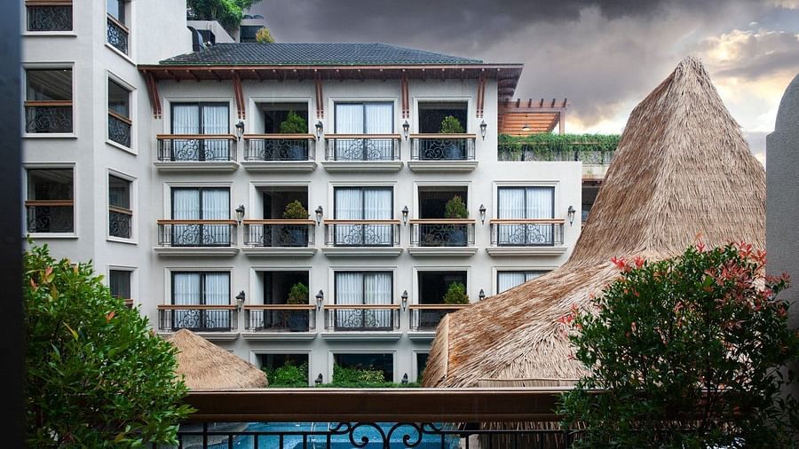 An exterior view of the multi-story hotel building at The Evren, Vagator, with a view of balconies and the swimming pool below. The image shows the building's architecture and the surrounding tropical environment under a dramatic sky.