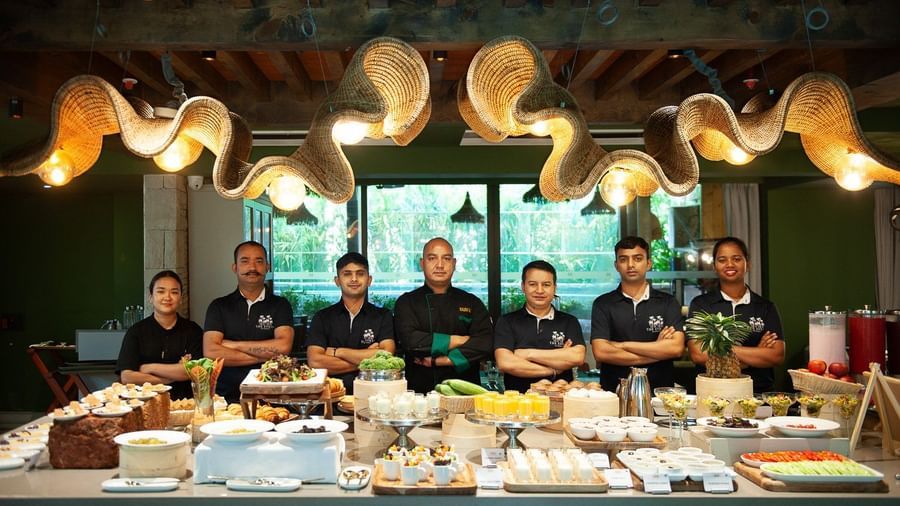  The culinary and service team of Mila Restaurant at The Evren, Vagator, standing proudly behind a beautifully presented buffet spread. The team is smiling and wearing their uniforms, with the head chef in the center.