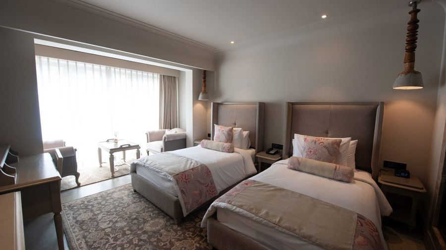 A wide-angle shot of a Premium Twin Room at The Evren, Vagator, showing two comfortable single beds, a desk, and a seating area with two armchairs and a coffee table near the large window.