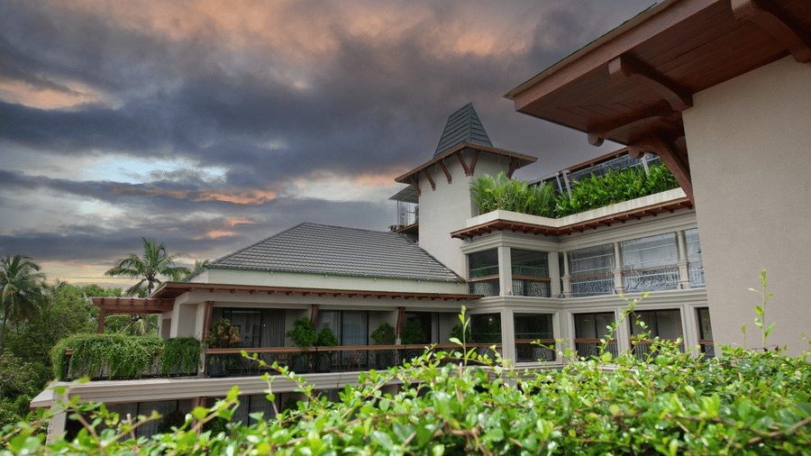 The exterior of The Evren, Vagator, showing the elegant facade, balconies, and the lush green surroundings against a dramatic sky.