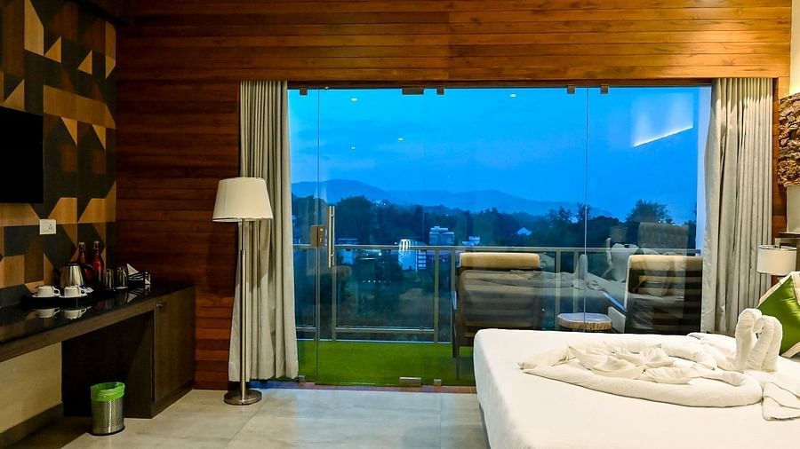 A hotel bedroom with a large bed, a bedside lamp, and an expansive view from a large glass door, suggesting access to a private balcony or terrace - Sea Hills Hotels, Sri Vijaya Puram (Port Blair)