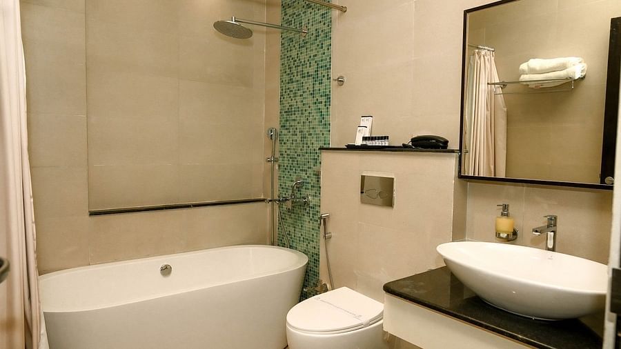A hotel bedroom with a large bed, a television, and bedside tables with lamps, featuring warm lighting and a mix of wooden and textured wall finishes - Sea Hills Hotels, Sri Vijaya Puram (Port Blair)