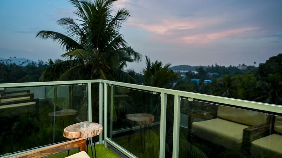 A spacious hotel balcony with a glass railing and outdoor seating, offering a view of palm trees and the sky at dusk or dawn - Sea Hills Hotels, Sri Vijaya Puram (Port Blair)