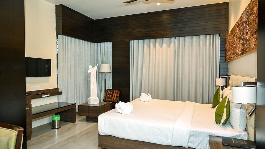 A hotel room with a large bed, bedside lamps, and a ceiling fan, with heavy curtains drawn, suggesting a cosy interior - Sea Hills Hotels, Sri Vijaya Puram (Port Blair)