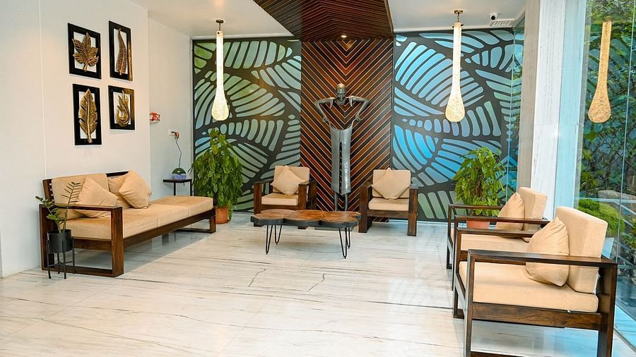A wide shot of a hotel lobby or lounge area featuring light-coloured sofas, wooden accents, and a distinctive patterned wall behind a decorative light fixture - Sea Hills Hotels, Sri Vijaya Puram (Port Blair)