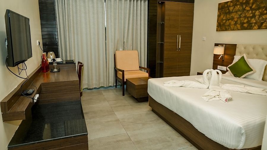 A hotel bedroom with a large bed, a television, and a small seating area, showcasing modern furnishings and a view towards the window - Sea Hills Hotels, Sri Vijaya Puram (Port Blair)