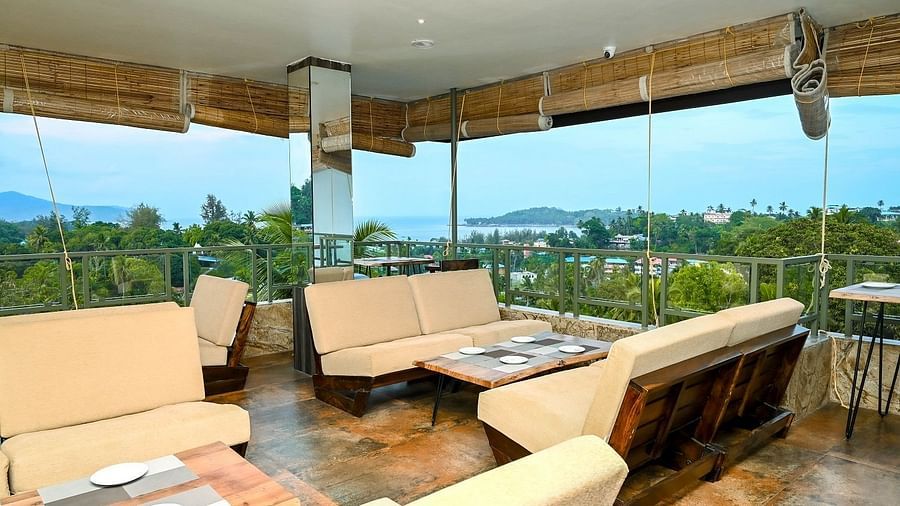 A closer view of an outdoor dining or lounge setup on a balcony, featuring a table with chairs and a picturesque background of greenery and water - Sea Hills Hotels, Sri Vijaya Puram (Port Blair)