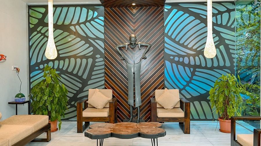 A close-up of a hotel lounge area with two wooden chairs, a low table, and a striking teal and brown patterned wall with hanging decorative elements - Sea Hills Hotels, Sri Vijaya Puram (Port Blair)