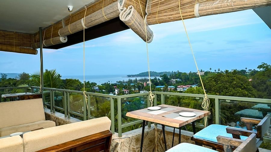 An expansive outdoor terrace or rooftop bar area with a long counter in the foreground and comfortable seating arranged to overlook a scenic landscape - Sea Hills Hotels, Sri Vijaya Puram (Port Blair)
