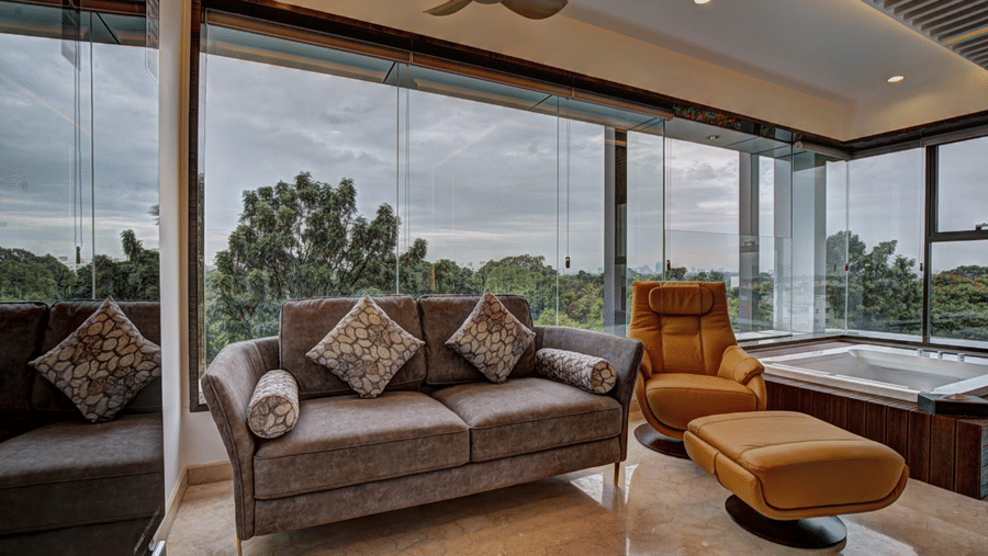 A 2-seater couch with cushions along with a reclining chair with a footrest in front of it at the Grand Suite of SRS Suites, Koramangala.