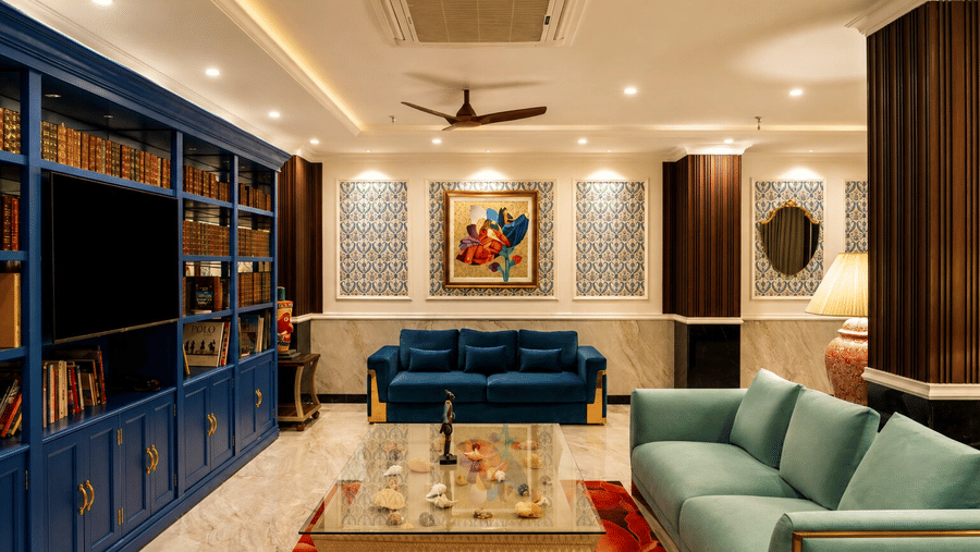 A lounge featuring blue sofas, a coffee table, and a large bookcase wall inside MAYFAIR Bay Resort, Paradeep.