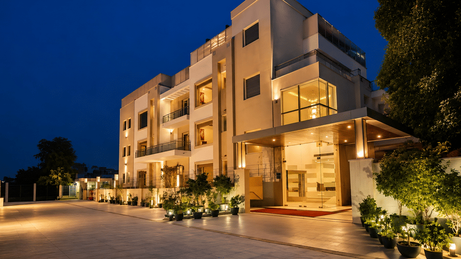 Hotel building exterior at night with an illuminated glass entrance, landscaped shrubs and warm lighting spread along the whole driveway.