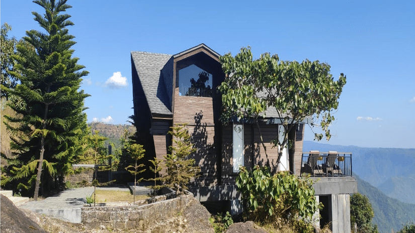 P Villa exterior at Polo Resort Cherrapunji, a pitched-roof timber villa perched on the cliff edge with pine trees, terrace seating and valley views.