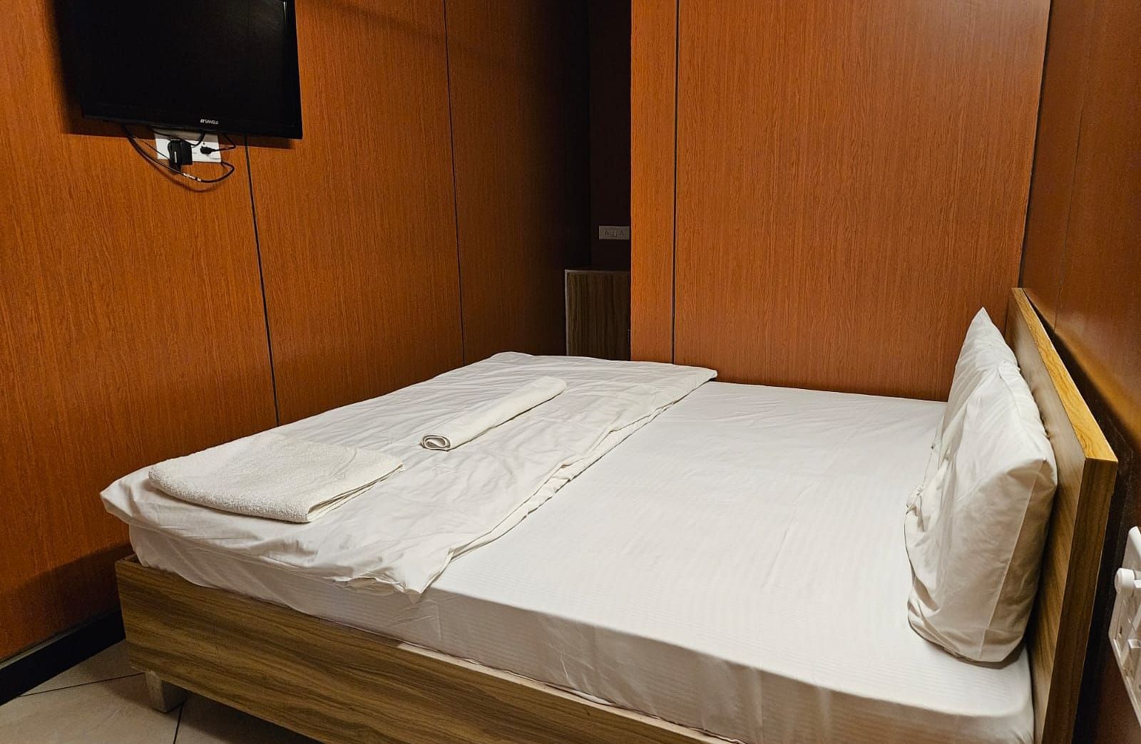 Corner view of a double bed with plain white bed sheet along with a wall mounted television at the Dream Vision Guest House.