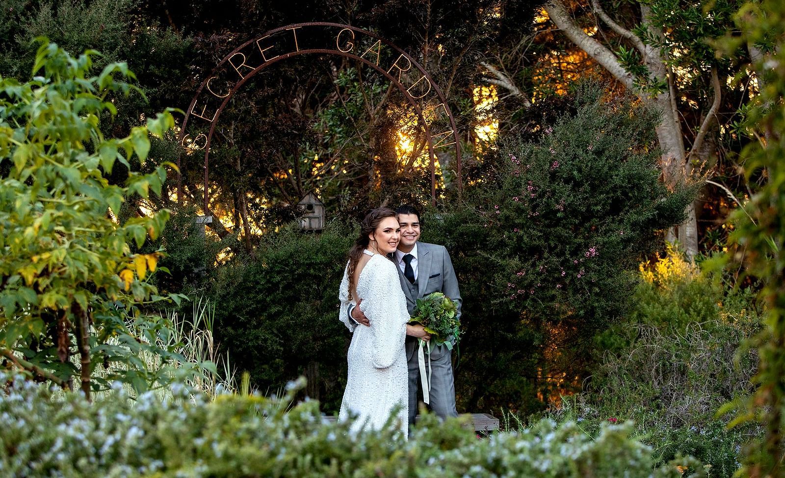 Newlyweds posing in a lush green garden under an enchanting archway