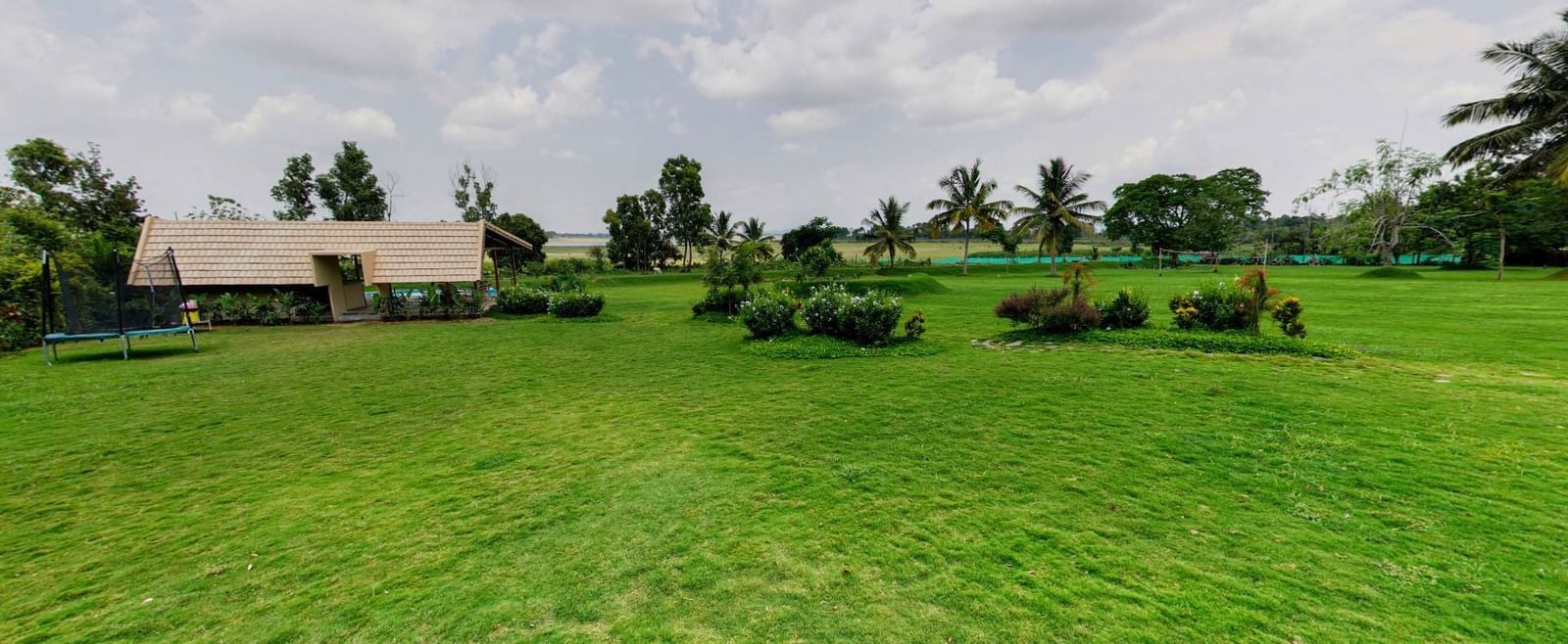 Expansive lawn with trimmed grass, scattered plants, and a single-storey building in the distance at Fireflies Resorts, Kabini.