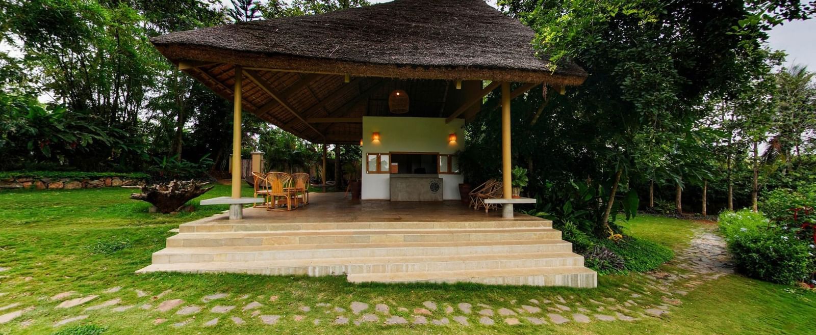 Open wooden reception area with steps and tiled flooring surrounded by greenery at Fireflies Resorts, Kabini.