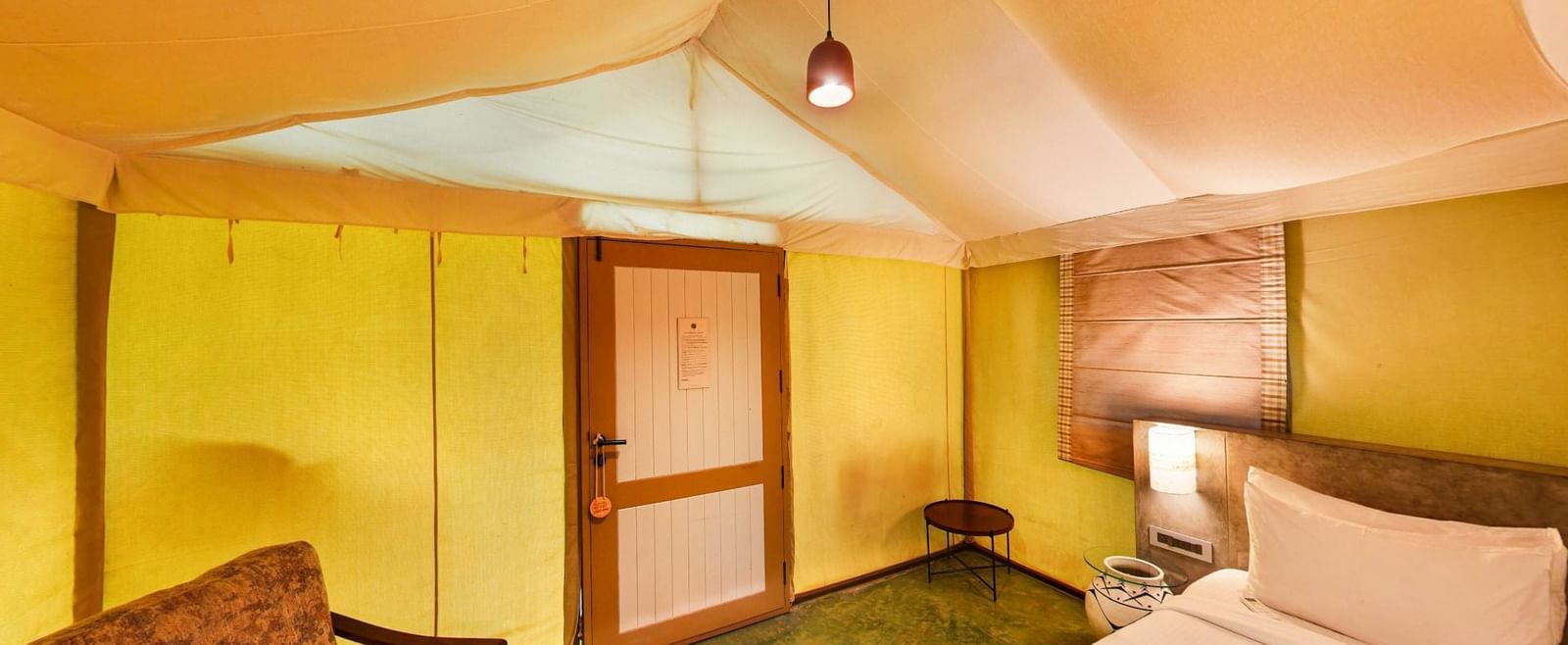 Tent room with sloped ceiling, king size bed, and wooden furniture beside the door at Fireflies Resorts, Kabini.
