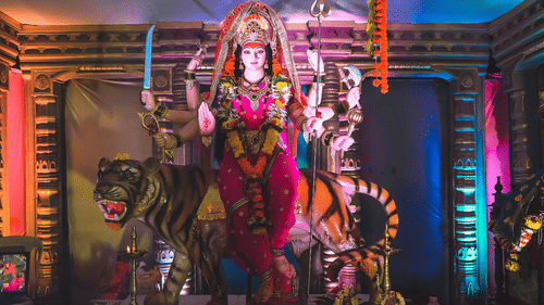 A decorated statue of a deity on a stage with colorful lights and figures around it.