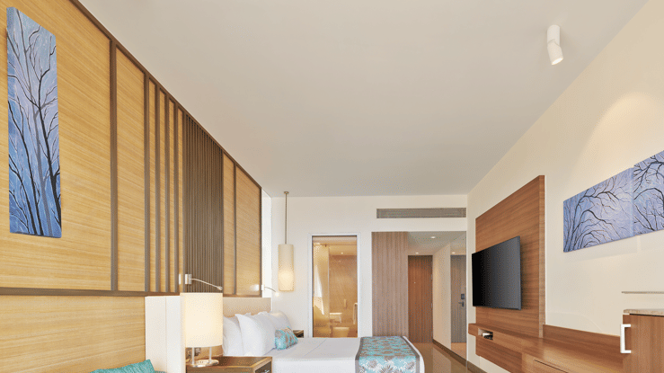 Stylish modern room with wooden accents, pastel furnishings, a wall-mounted TV and an open layout leading to a spacious ensuite – The Resort, Mumbai.
