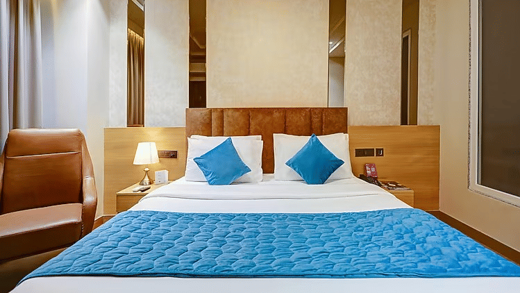 A bedroom at Hotel 91 HUDA Premier, Gurugram with a king size bed, runner, pillows, headboard, bedside lamps, and armchair.