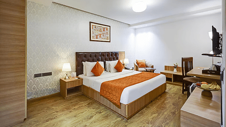 A well-lit guest room showing a double bed, a dedicated wooden study desk with a chair, and large windows - Hotel 91 HUDA City Centre, Gurugram