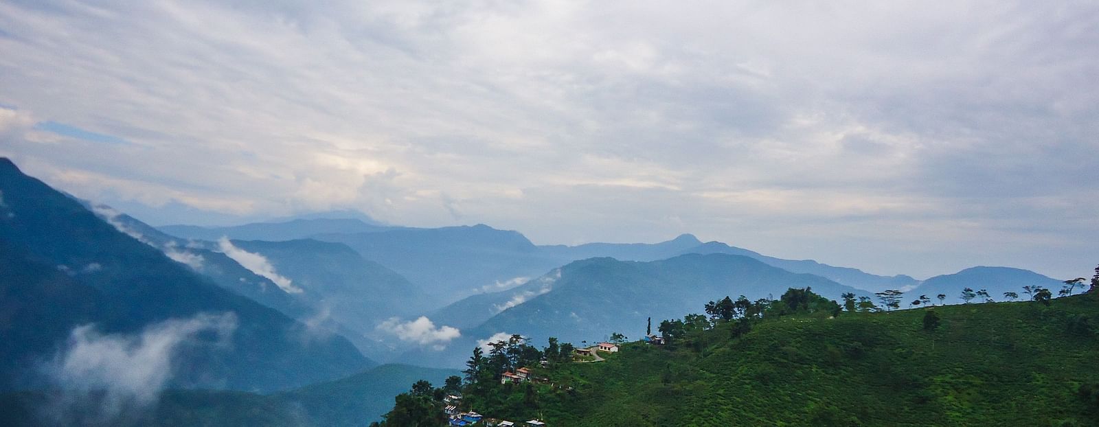 An image of hills with greenery where clouds are hovering on top and a beautiful sky