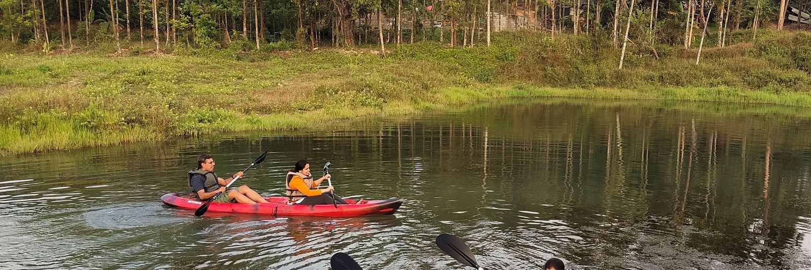 People in life jackets paddling kayaks on a serene river with dense forest in the background - Evergreen County