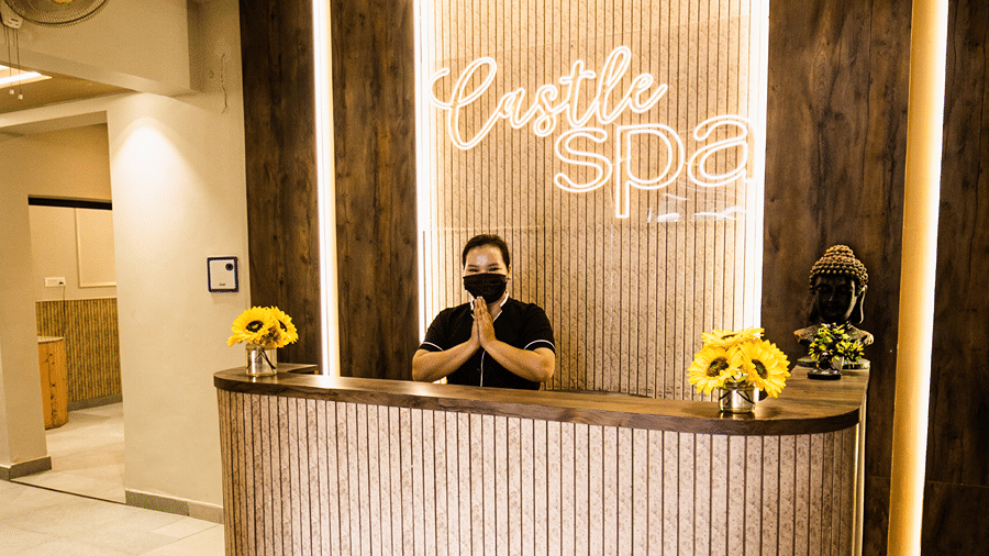 A modern spa reception desk with warm ambient lighting and a staff member waiting behind the counter - Wood Castle Spa & Resort, Jim Corbett