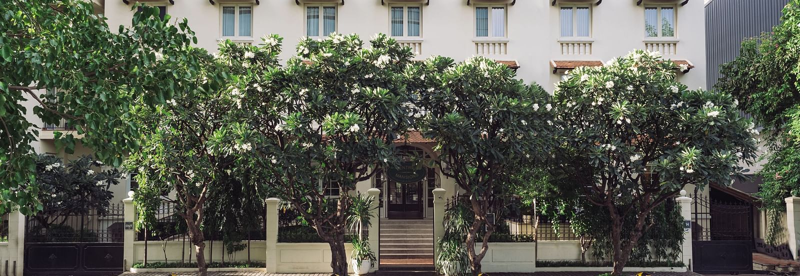 A multi-storey building with a distinctive roof line, framed by foliage | Central Mansions, Phnom Penh