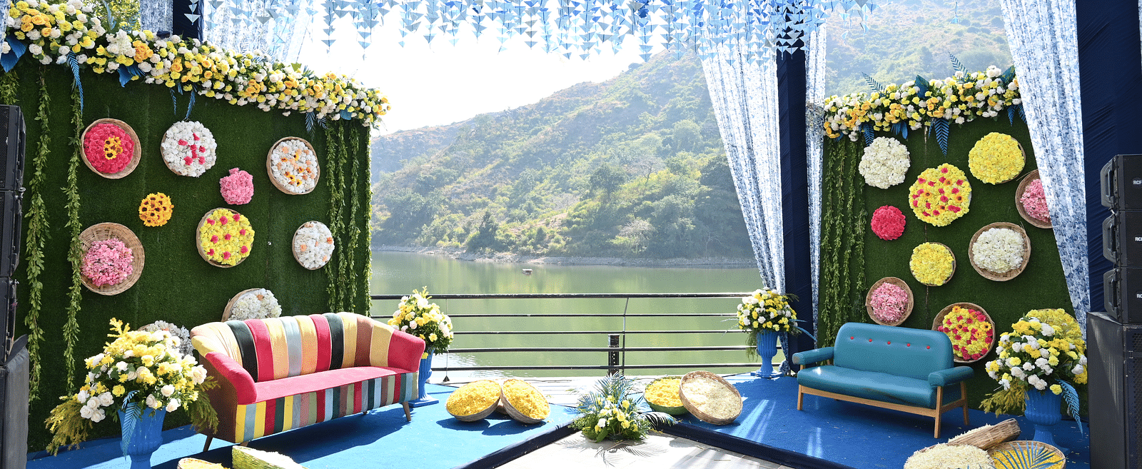 Blue floral mandap with colourful sofa seating and green hills as a backdrop - Via Lakhela Resort & Spa