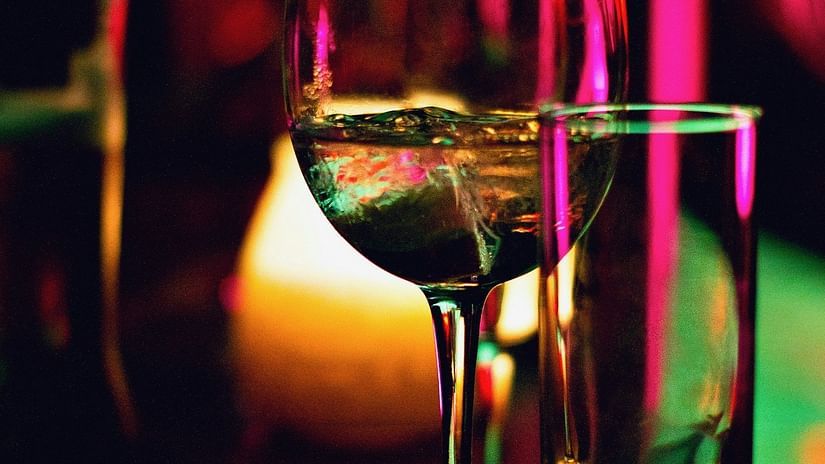 Wine glass and tumblers on a bar, illuminated by vibrant lights, creating a lively atmosphere.